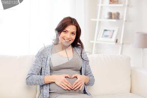 Image of happy pregnant woman making heart gesture at home