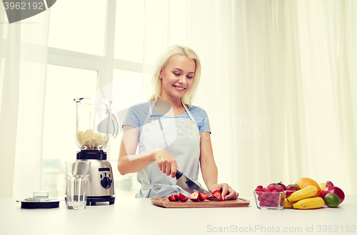 Image of smiling woman with blender preparing shake at home