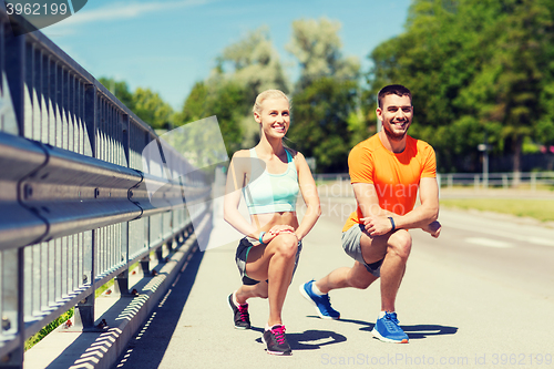 Image of smiling couple stretching leg outdoors