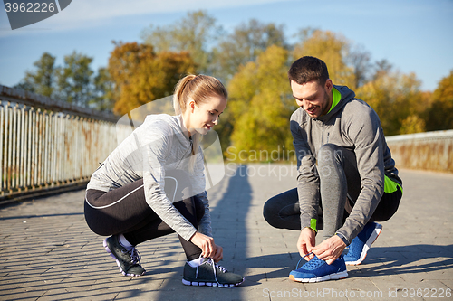 Image of smiling couple tying shoelaces outdoors