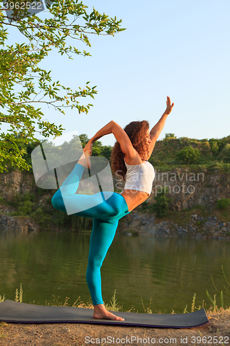 Image of Young woman is practicing yoga near river