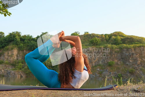 Image of Young woman is practicing yoga near river