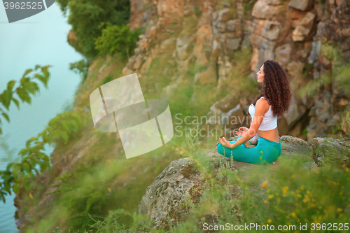 Image of Young woman is practicing yoga near river