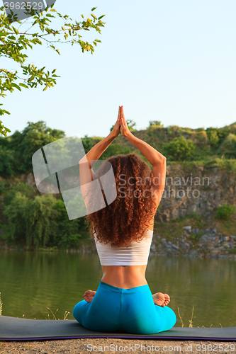 Image of Young woman is practicing yoga near river