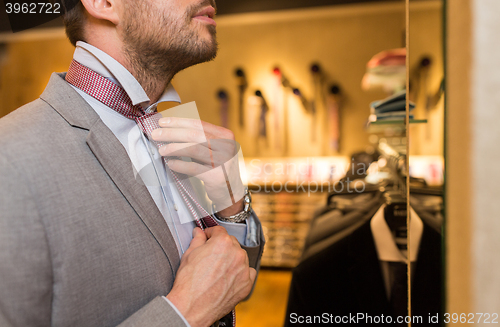 Image of close up of man tying tie at clothing store mirror