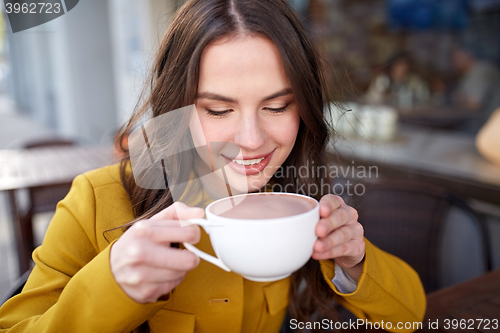 Image of happy woman drinking cocoa at city street cafe