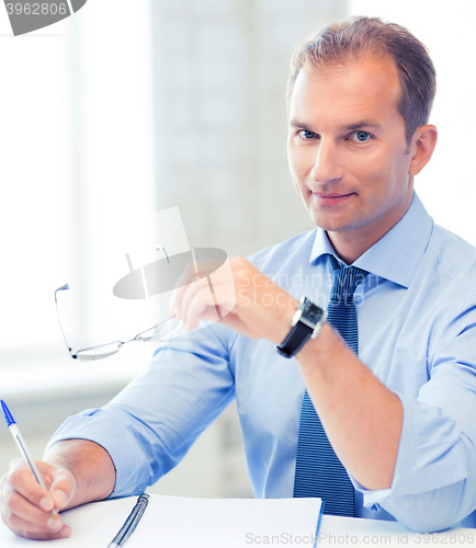 Image of businessman with spectacles writing in notebook