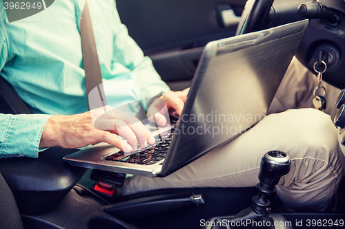 Image of close up of young man with laptop driving car