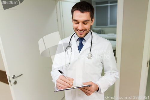 Image of happy doctor writing to clipboard at hospital