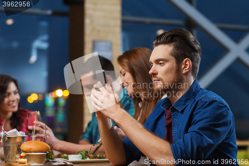 Image of man with smartphone and friends at restaurant