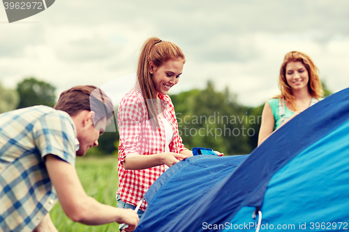 Image of group of smiling friends setting up tent outdoors