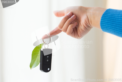 Image of close up of hand holding car key with green leaf