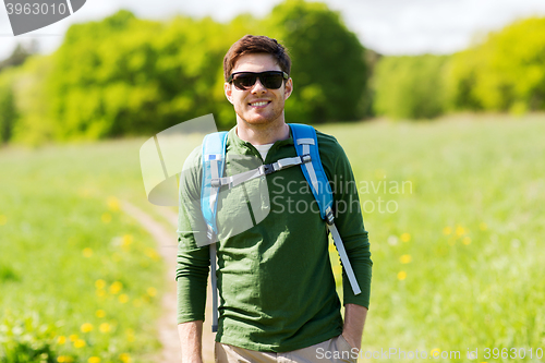 Image of happy young man with backpack hiking outdoors