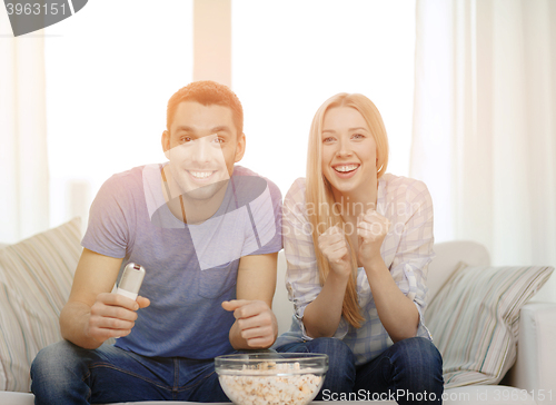 Image of smiling couple with popcorn cheering sports team