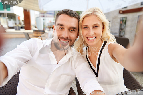 Image of happy couple taking selfie at restaurant terrace