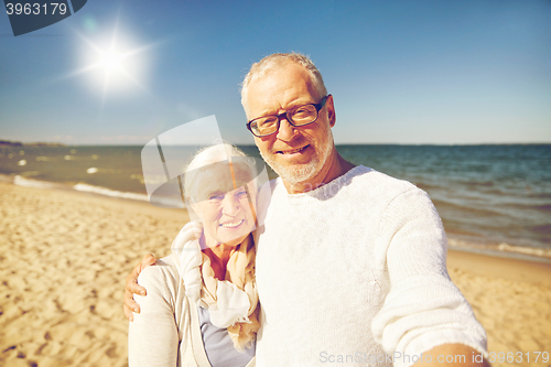 Image of seniors taking picture with selfie stick on beach