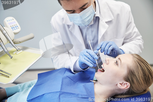 Image of male dentist in mask checking female patient teeth