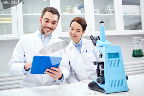 Image of scientists with tablet pc and microscope in lab