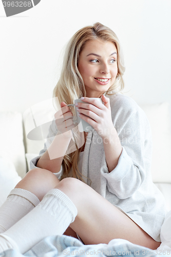 Image of happy woman with cup of coffee in bed at home