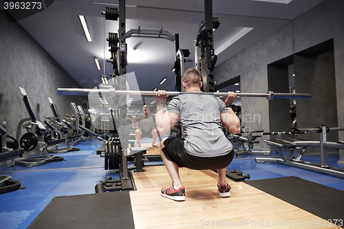 Image of young man flexing muscles with bar in gym