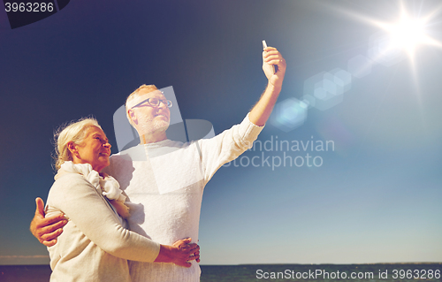 Image of seniors with smartphone taking selfie on beach