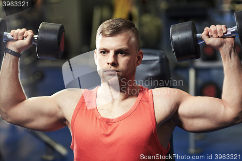 Image of young man with dumbbells flexing muscles in gym