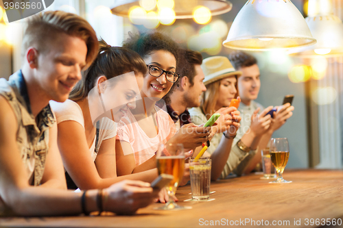Image of happy friends with smartphones and drinks at bar