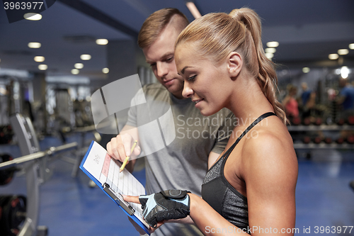 Image of smiling woman with trainer and clipboard in gym