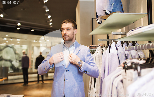 Image of happy young man trying suit at clothing store