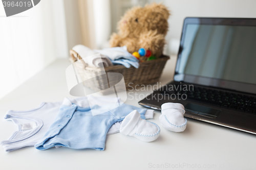 Image of close up of baby clothes, toys and laptop at home