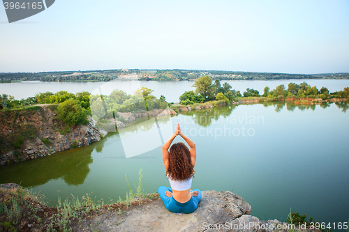 Image of Young woman is practicing yoga near river