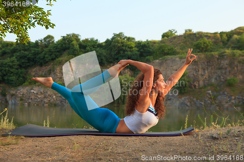 Image of Young woman is practicing yoga near river