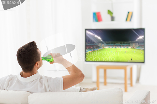 Image of man watching soccer game on tv and drinking beer