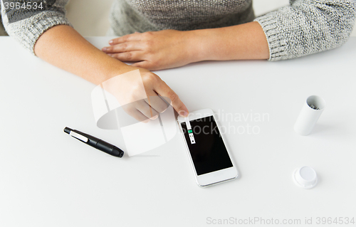 Image of close up of woman with smartphone doing blood test
