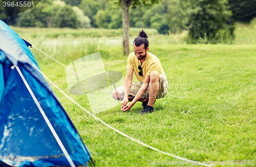 Image of happy man setting up tent outdoors