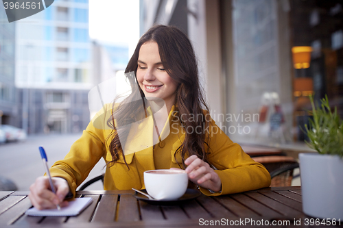 Image of happy woman with notebook drinking cocoa at cafe