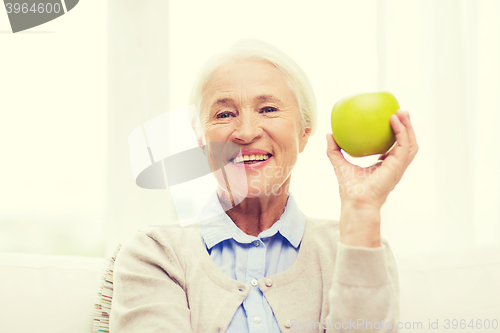 Image of happy senior woman with green apple at home