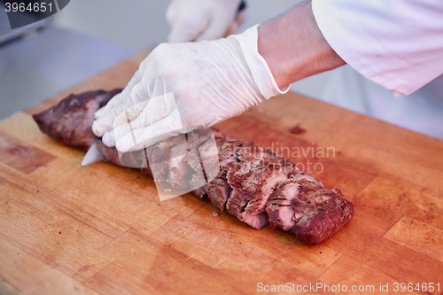 Image of Male chef cutting big piece of beef on wooden board