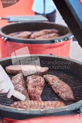 Image of thick strip steak being grilled outdoors. Shallow dof