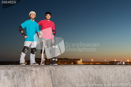 Image of Two skateboarders standing near a concrete pool 