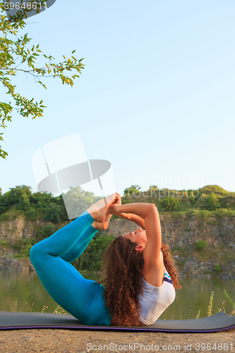 Image of Young woman is practicing yoga near river