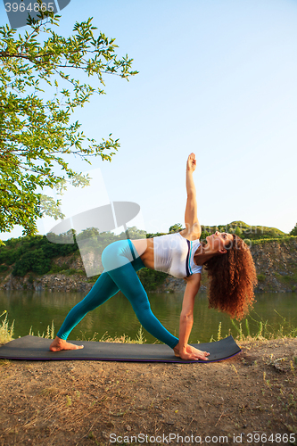 Image of Young woman is practicing yoga near river