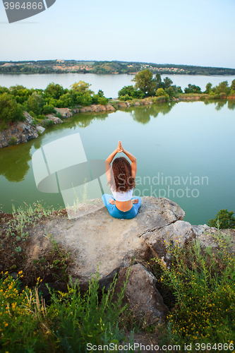 Image of Young woman is practicing yoga near river