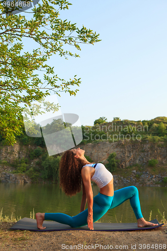 Image of Young woman is practicing yoga near river