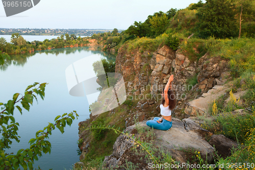 Image of Young woman is practicing yoga near river