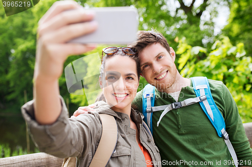 Image of couple with backpacks taking selfie by smartphone