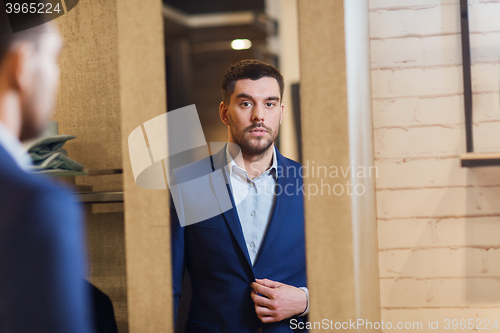 Image of man trying jacket on at mirror in clothing store