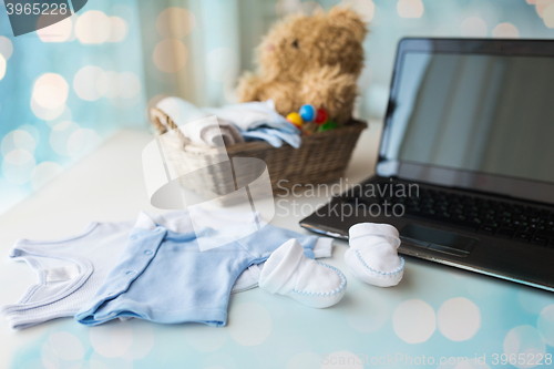 Image of close up of baby clothes, toys and laptop at home