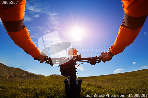 Image of Hands in orange jacket holding handlebar of a bicycle