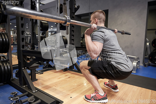 Image of young man flexing muscles with bar in gym